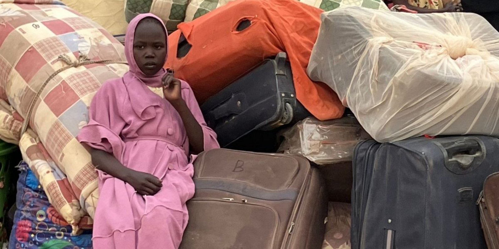 Ein Mädchen aus dem Südsudan sitzt auf einem Haufen Taschen und Koffern