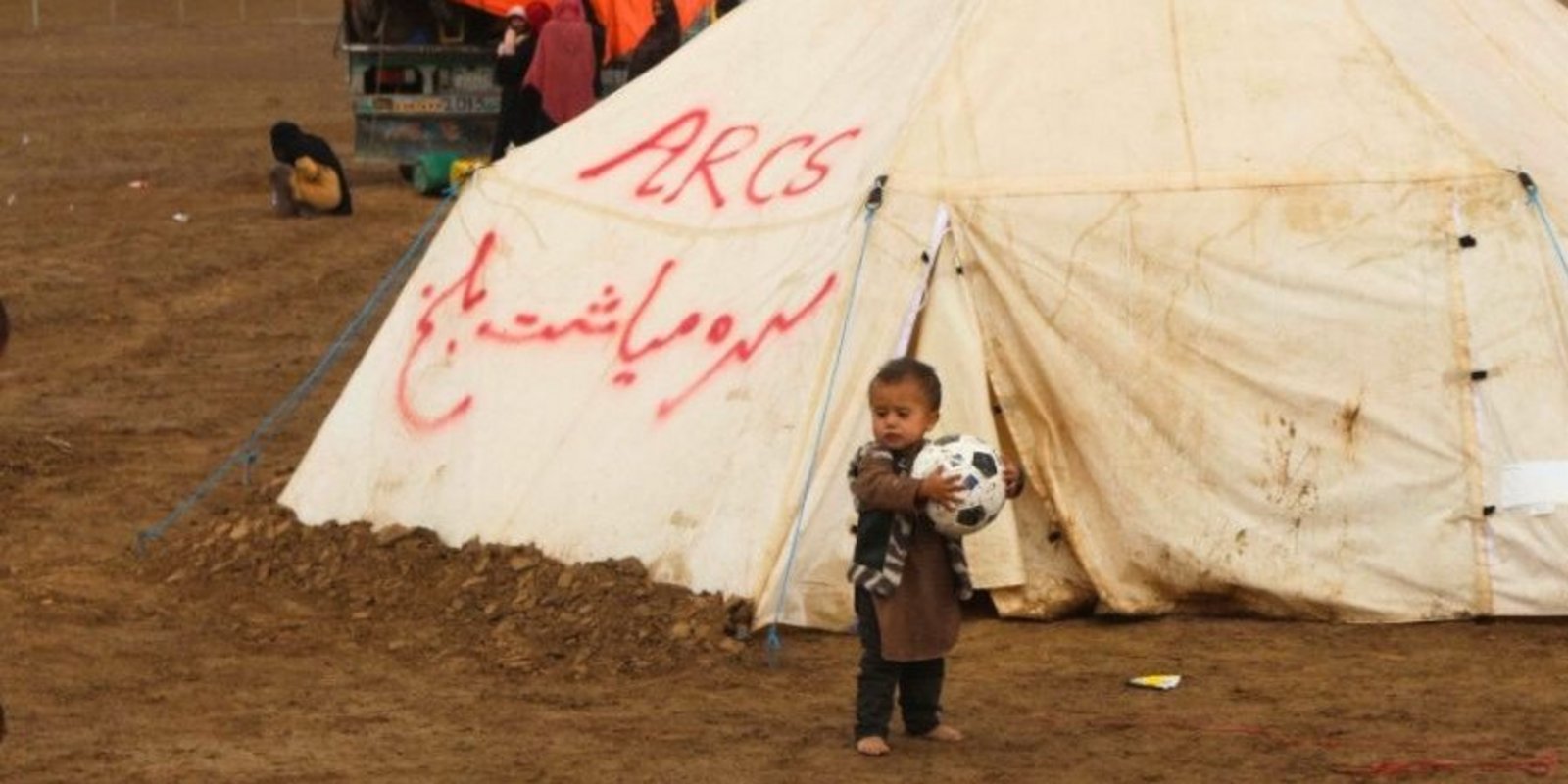 Ein Kind steht allein auf einem Feld vor einem Flüchtlingszelt