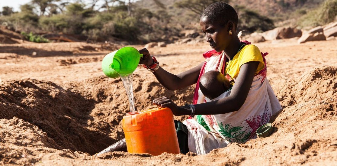Frau mit Baby an vertrockneter Wasserstelle in Kenia